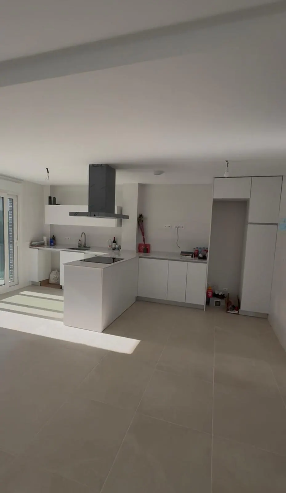 A bright, modern kitchen with white cabinets, a gray range hood, and a large island. Sunlight streams in from a window.
