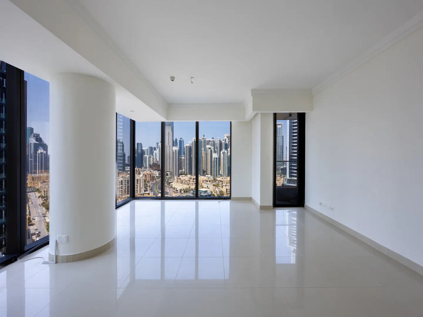 Empty, bright room with white walls and tile floors. Large windows offer a city view.