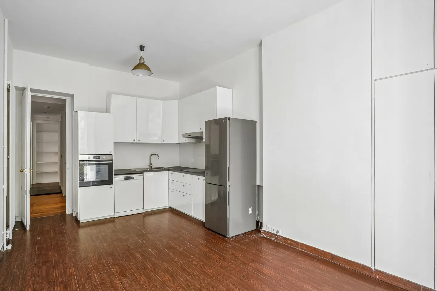 A bright kitchen with white cabinets, a stainless steel refrigerator, and dark wood floors.