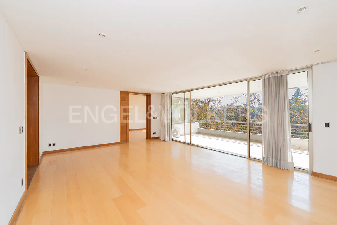 Spacious, bright room with light wood floors, white walls, and large sliding glass doors to a balcony with trees in the background.