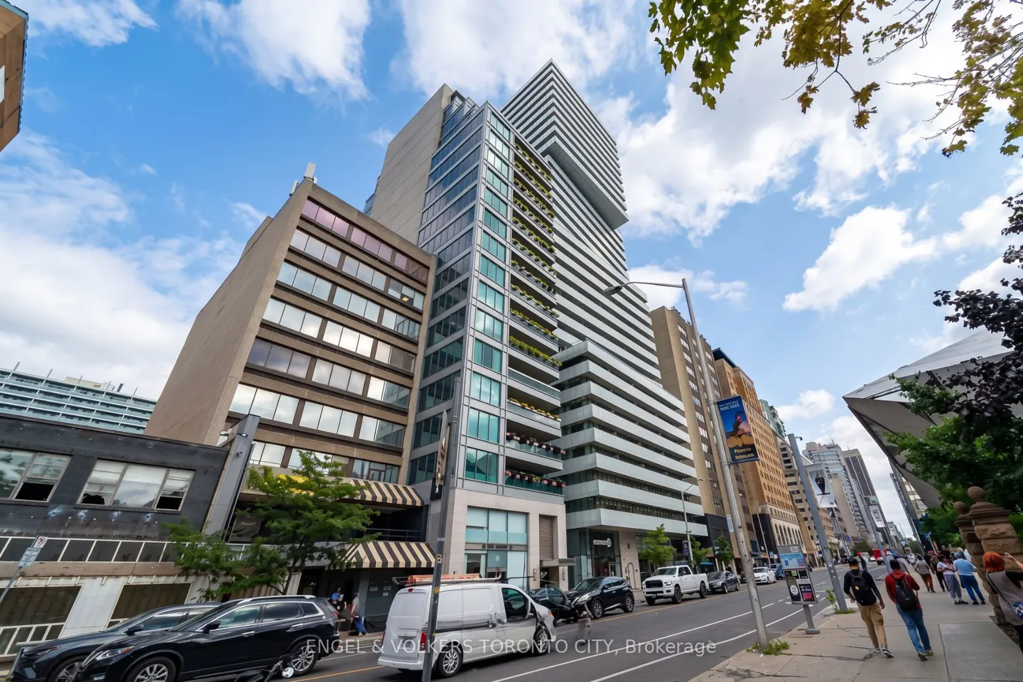 Low-angle view of a modern high-rise apartment building in a busy Toronto city street with cars and pedestrians.