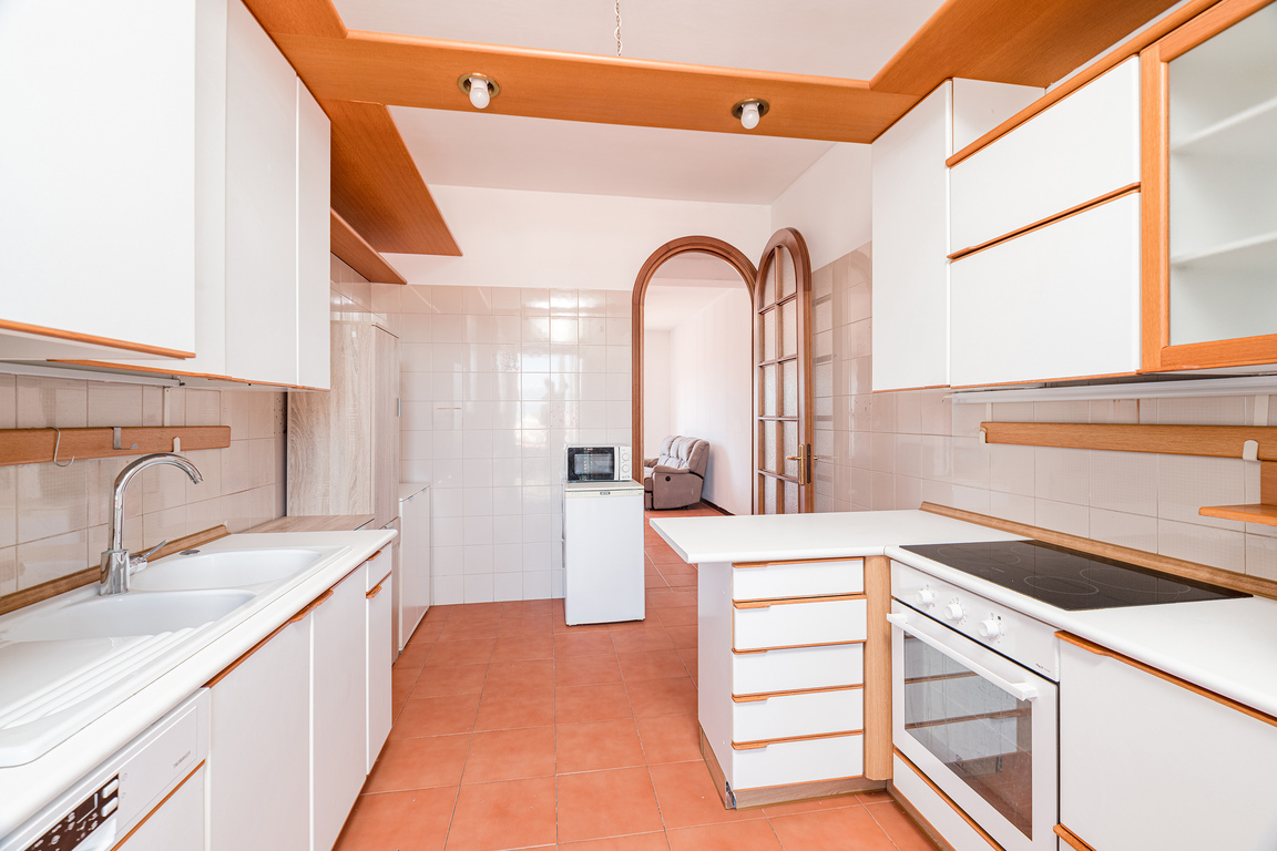 Kitchen with white cabinets, wood trim, terracotta tile floors, a double sink, and an arched doorway to a living area.