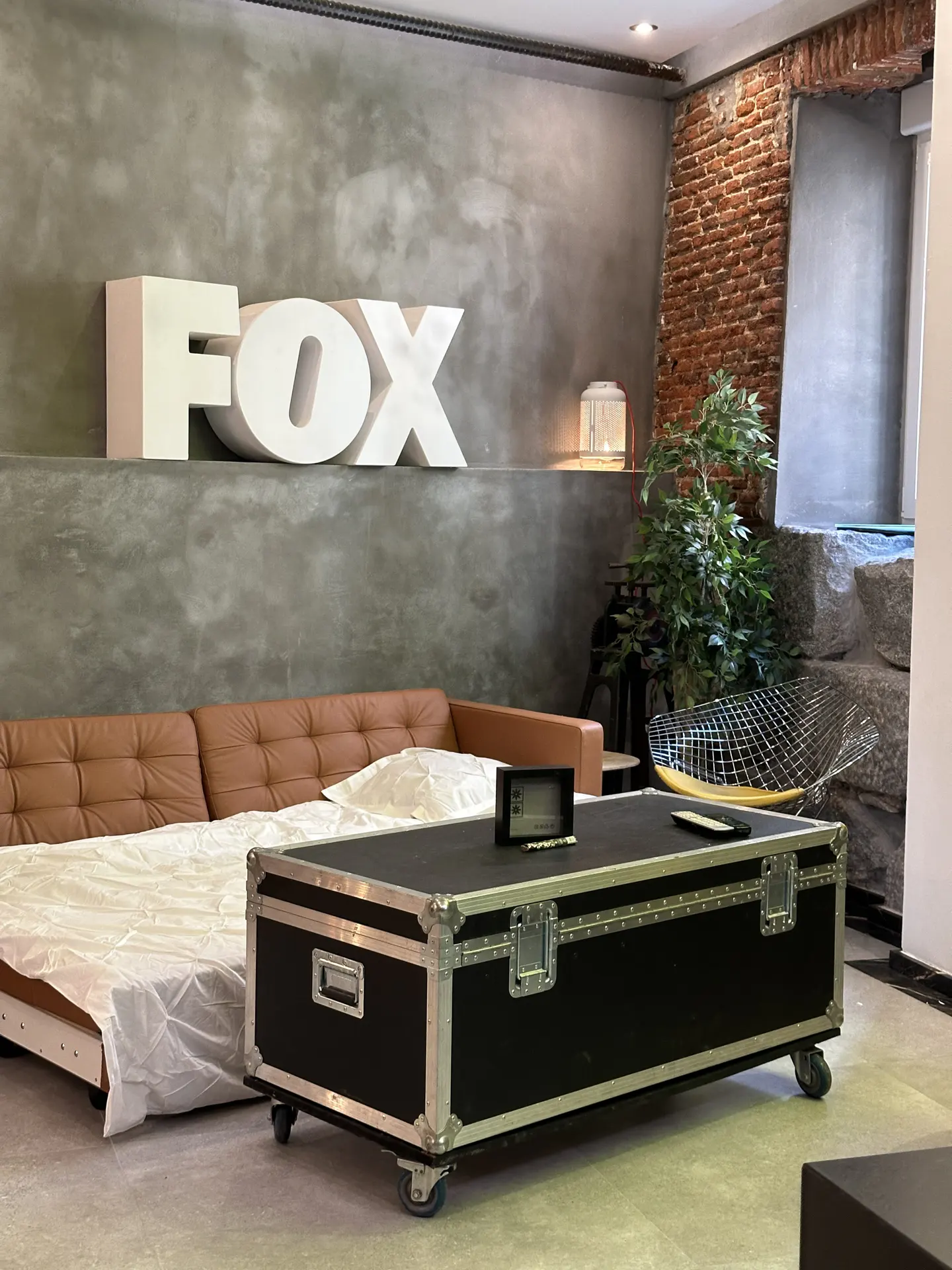 Living room with a brown leather sofa, a black trunk-style coffee table, and a large "FOX" sign on the wall.