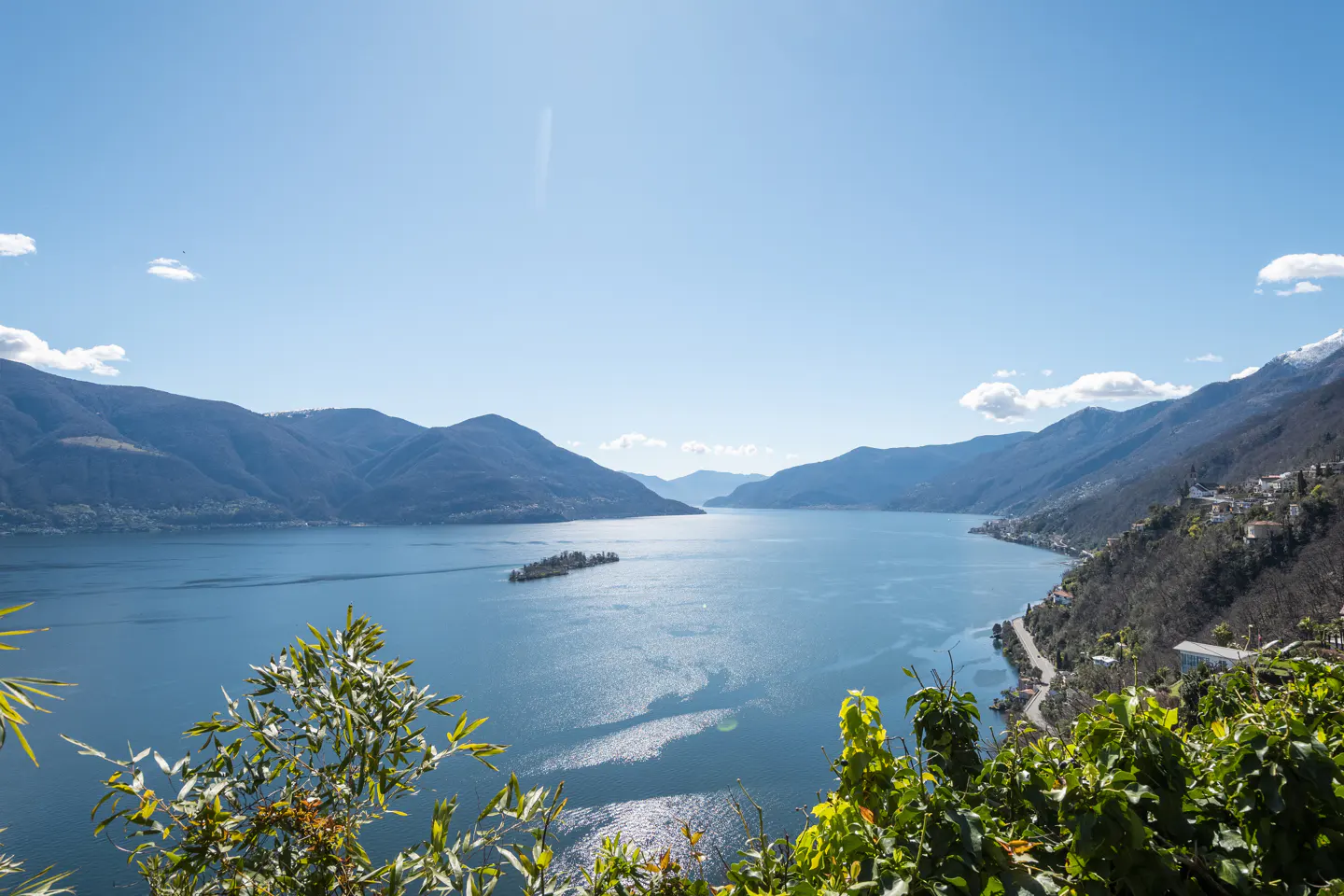 Scenic view of Lake Lugano, Switzerland, with blue water, green mountains, and a small island under a clear blue sky.