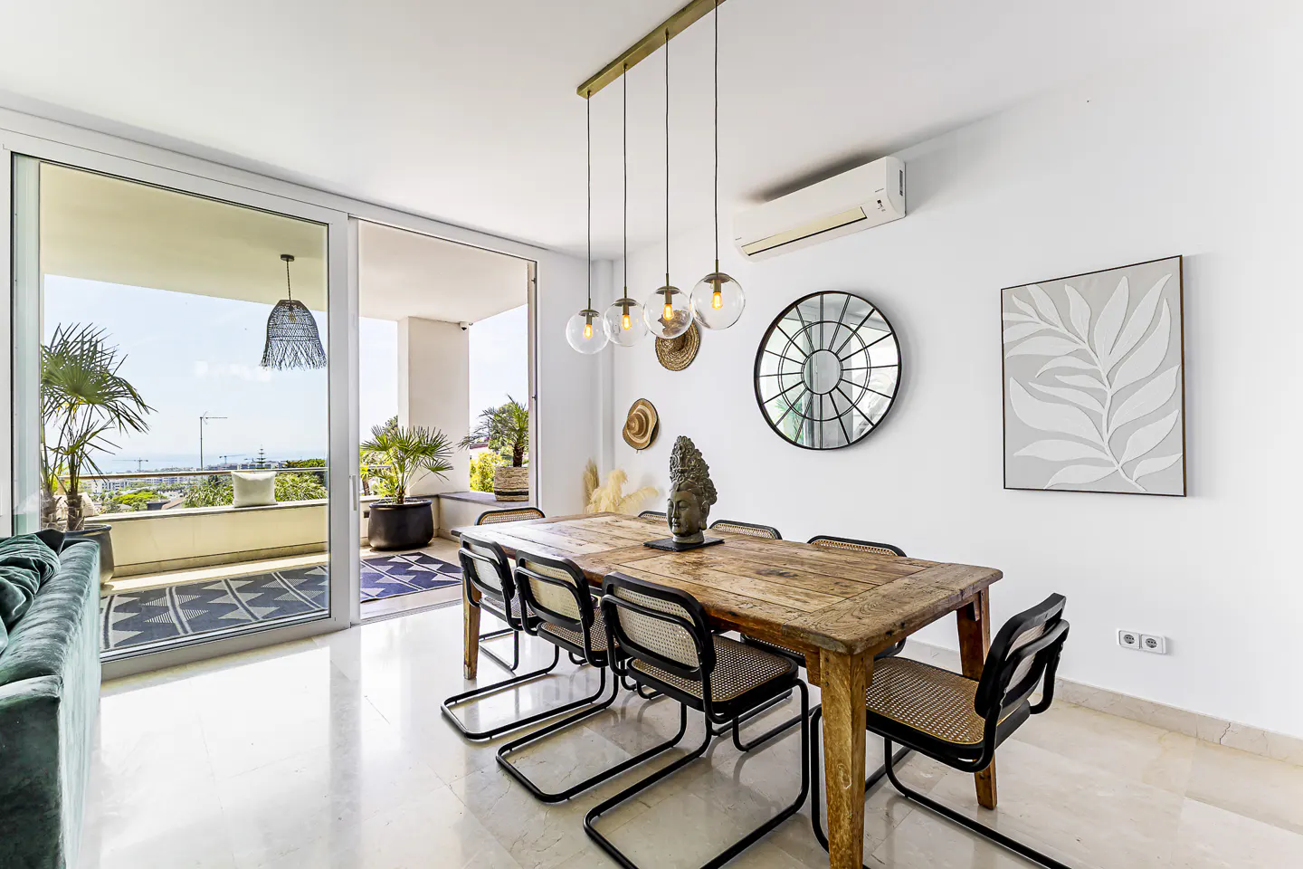 Bright dining room with a rustic wood table, black chairs, and a balcony view. Globe pendant lights hang above.