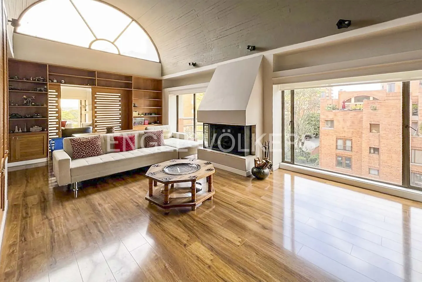 Living room with hardwood floors, a white sofa, a fireplace, and a large window with a view of a brick building.