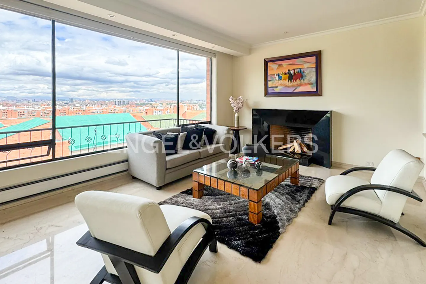 Modern living room with a grey sofa, two white armchairs, a glass coffee table, and a black fireplace with city views.