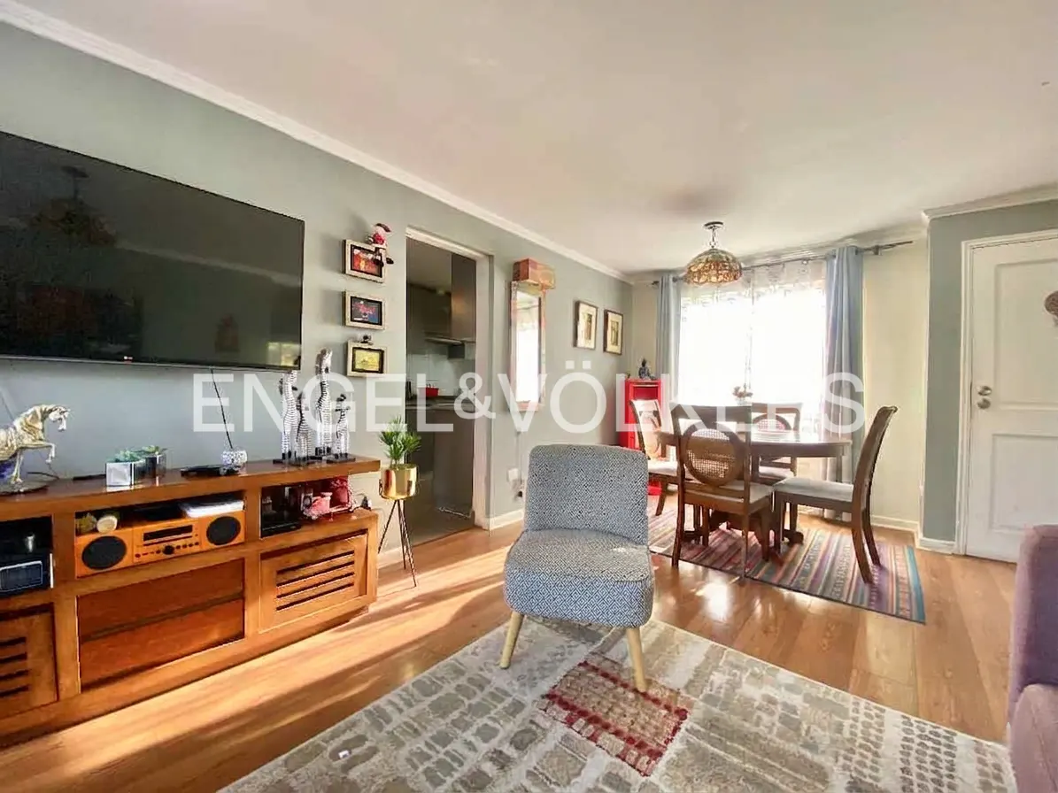 Living room with wood floors, a TV on a wood cabinet, a patterned chair, and a dining table with chairs.