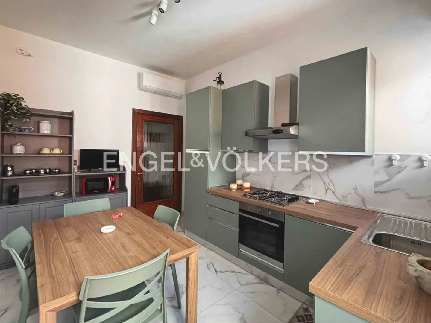 A kitchen with gray cabinets, a wooden countertop, and a wooden table with green chairs.
