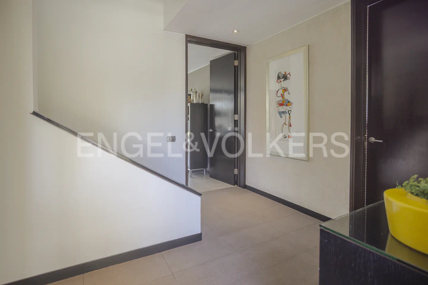 Hallway with stairs, a dark door, and an abstract art piece on the wall. A yellow planter sits on a black table.