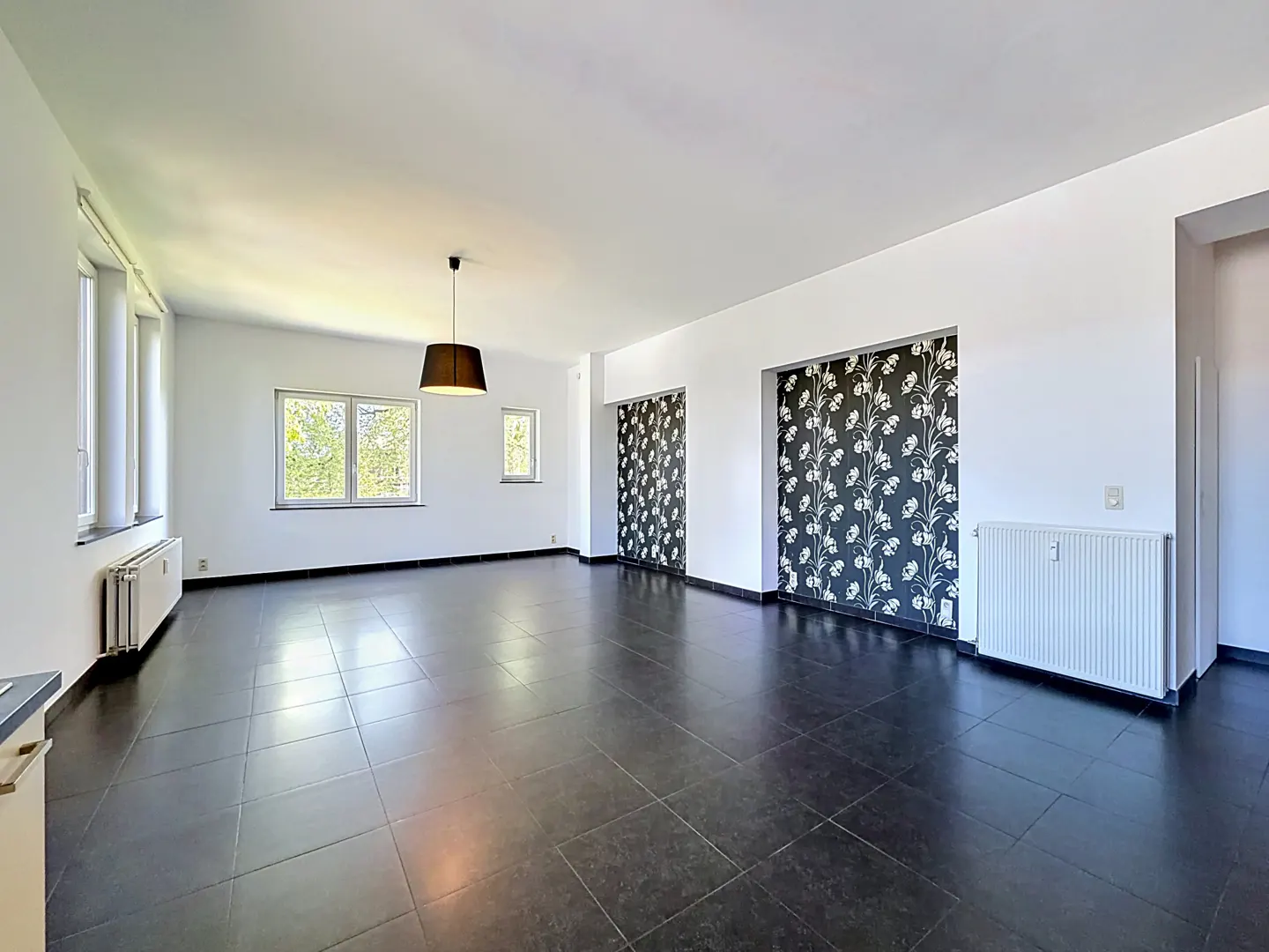 Bright, empty room with black tile floor, white walls, and floral wallpaper on two inset sections. Windows let in natural light.