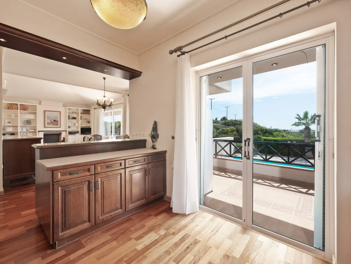 Interior view of a home with wood floors, cabinets, and sliding glass doors to a patio with a pool.