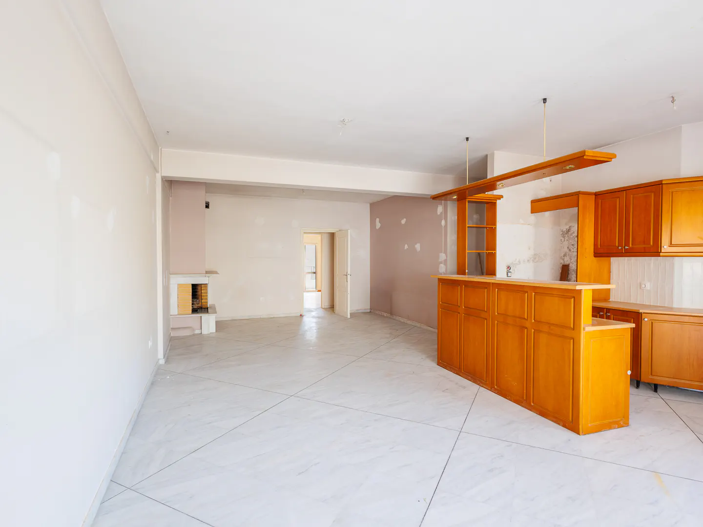 Open-plan living area with white tiled floors, light walls, a wooden kitchen island, and a fireplace in the background.