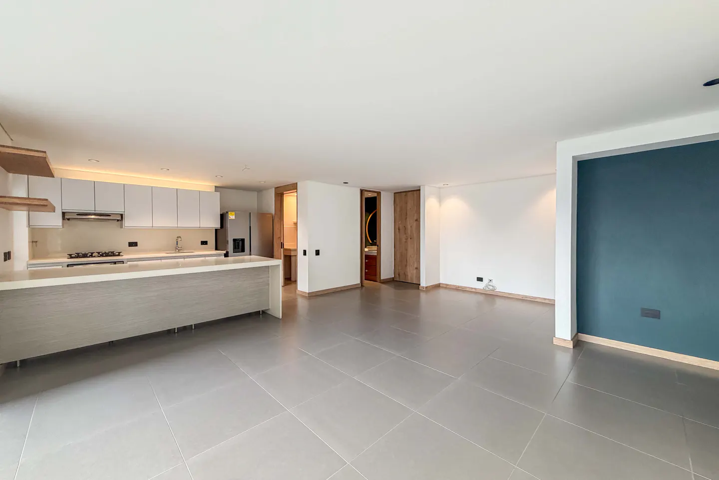 Open-concept living space with gray tile floors, white kitchen cabinets, and a large island. One wall is painted a dark teal color.