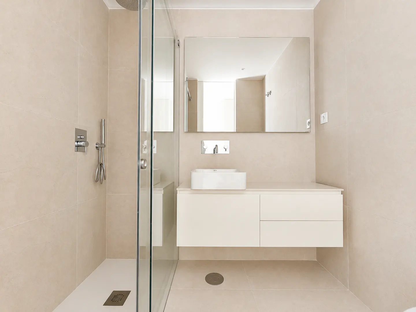 Modern bathroom with beige tile walls, glass shower, and white vanity with a rectangular sink and large mirror.