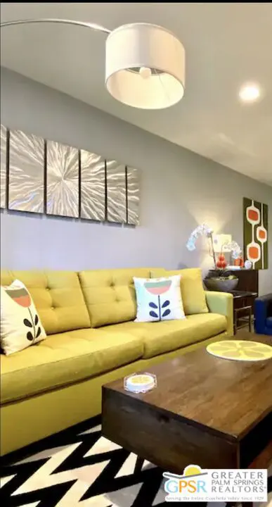Living room with a yellow sofa, wooden coffee table, and black and white zig-zag rug. Modern art hangs on the gray wall.