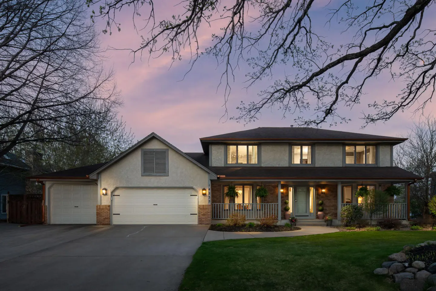 Two-story house with a two-car garage, a porch, and a green lawn at dusk.