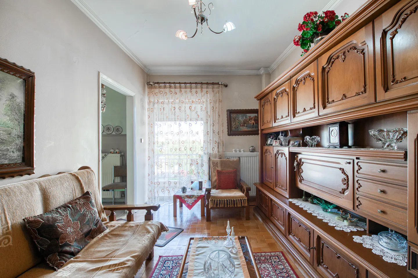 A living room with a beige sofa, a wooden cabinet, and a balcony with patterned curtains.