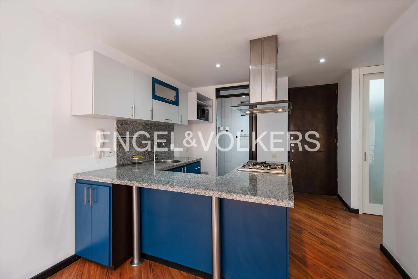 A modern kitchen with white cabinets, blue accents, and a granite countertop island. Stainless steel appliances and wood floors complete the space.