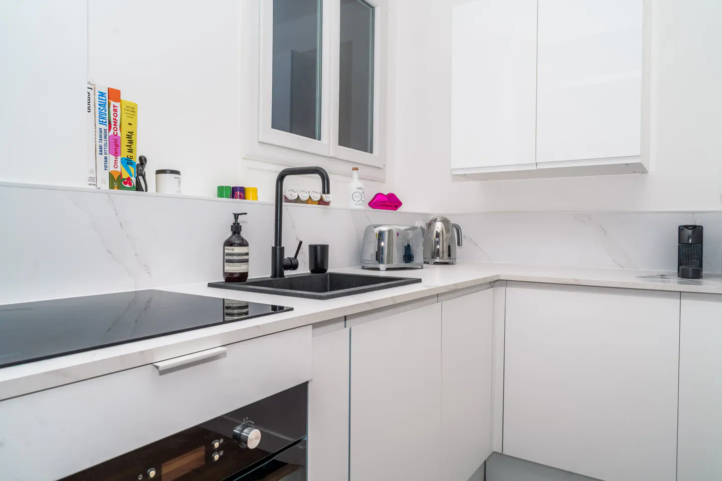 Bright, modern kitchen with white cabinets, marble countertops, and a black sink and faucet. A toaster and kettle sit on the counter.