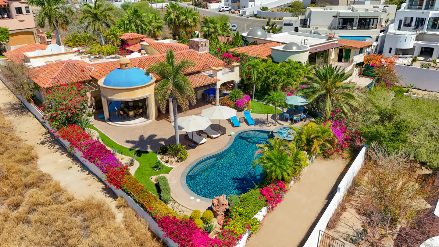 Aerial view of a luxury villa with a pool, red tile roof, and blue dome, surrounded by lush tropical landscaping.