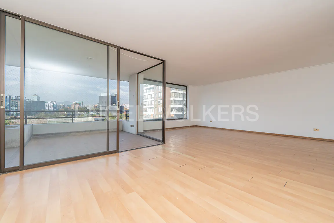 Empty living room with light wood floors, white walls, and large glass doors leading to a balcony with a city view.
