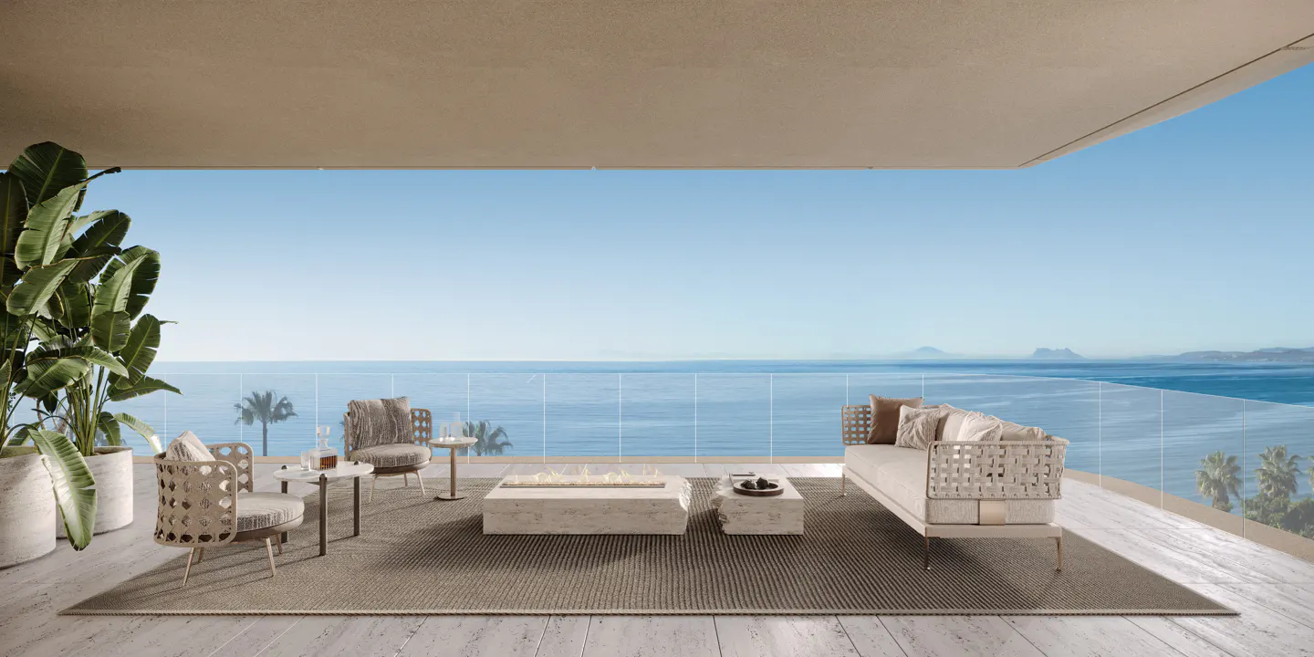 Luxury patio with ocean view. Beige sofa, chairs, and stone tables sit on a woven rug. Potted plant on the left.