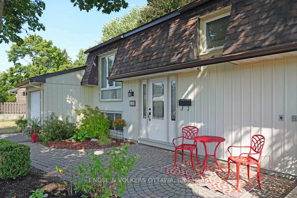 Exterior of a light yellow house with a brown roof, red patio set, and brick walkway.