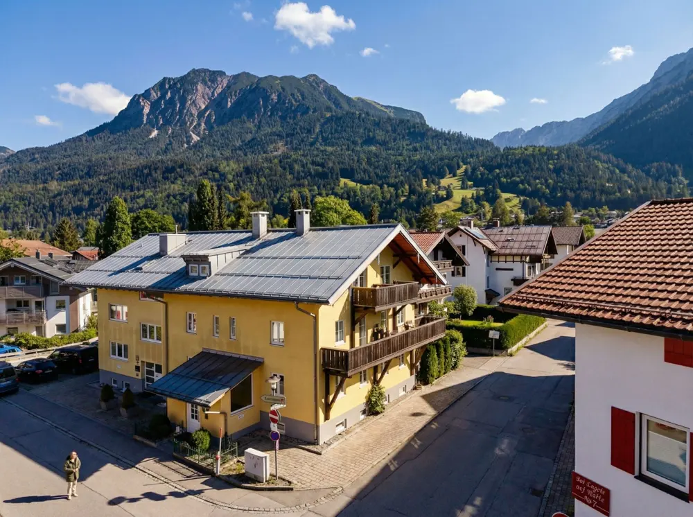 A yellow building with balconies sits in a town with mountains in the background.