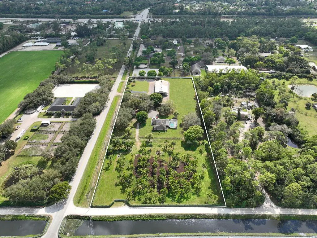 Aerial view of a large, green property outlined in white, featuring a house, pool, barn, and palm trees.