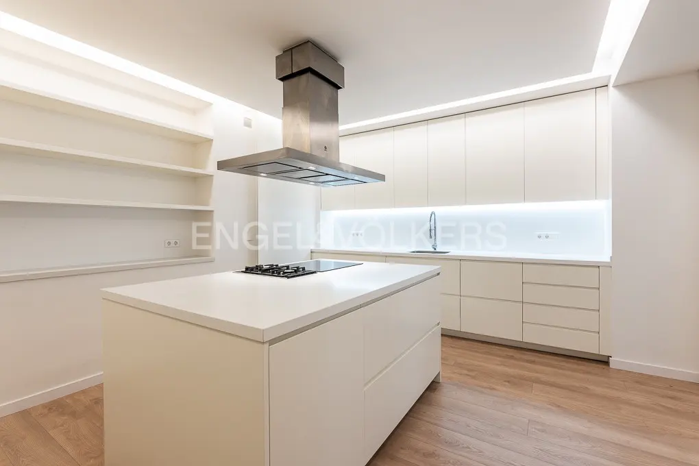 Bright, modern kitchen with white cabinets, island with cooktop, and stainless steel range hood. Wood floors and open shelving.