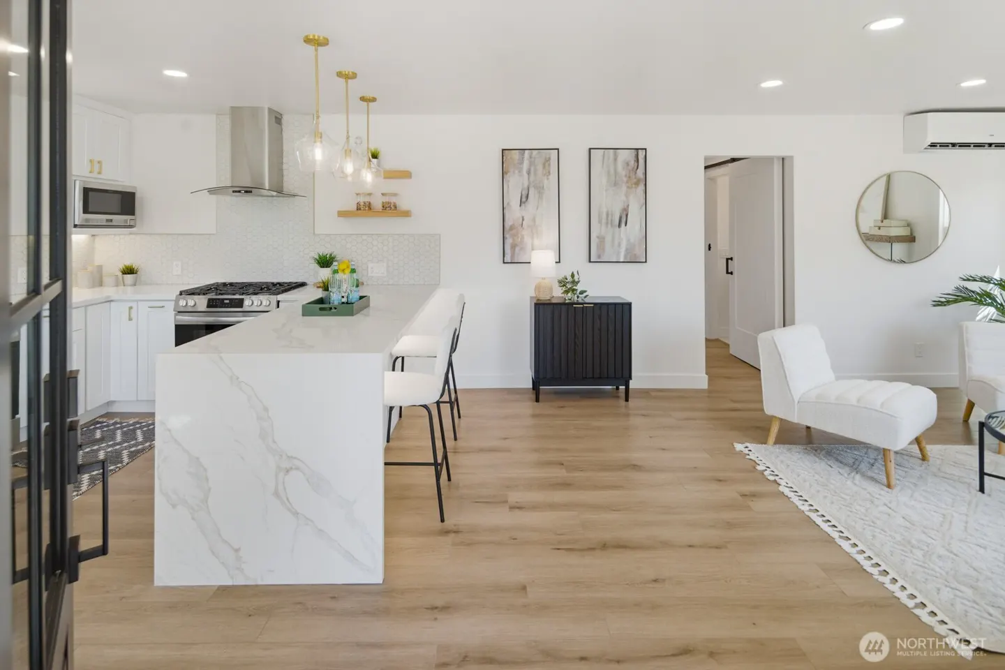 Bright, open-concept kitchen and living room with white cabinets, marble island, wood floors, and modern furniture.