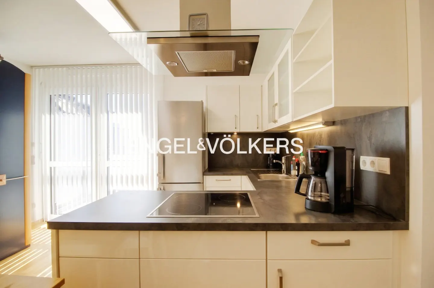 Bright kitchen with white cabinets, stainless steel appliances, and dark countertops. A coffee maker sits on the counter.