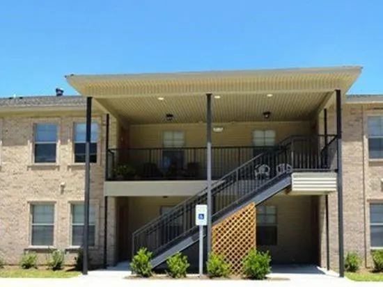 Two-story apartment building with beige brick, black stairs, and a covered porch. A handicap sign is visible.