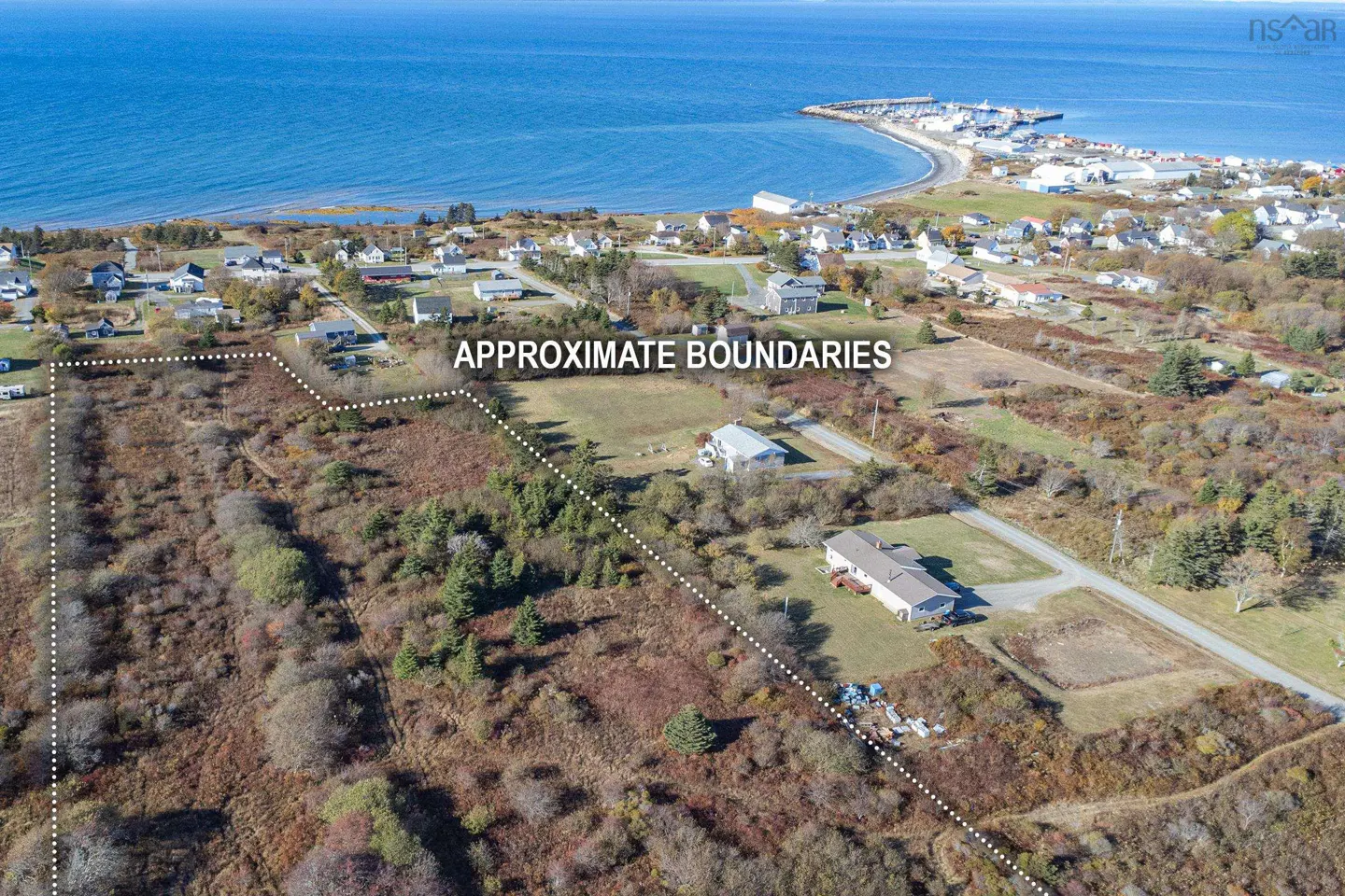 Aerial view of land for sale near the ocean, with dotted lines marking approximate boundaries. Houses and trees are visible.