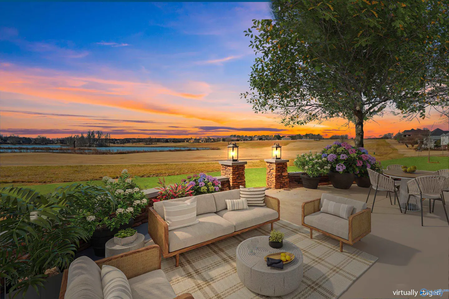 Outdoor patio with wicker furniture, a table, and chairs overlooking a green field and lake at sunset.