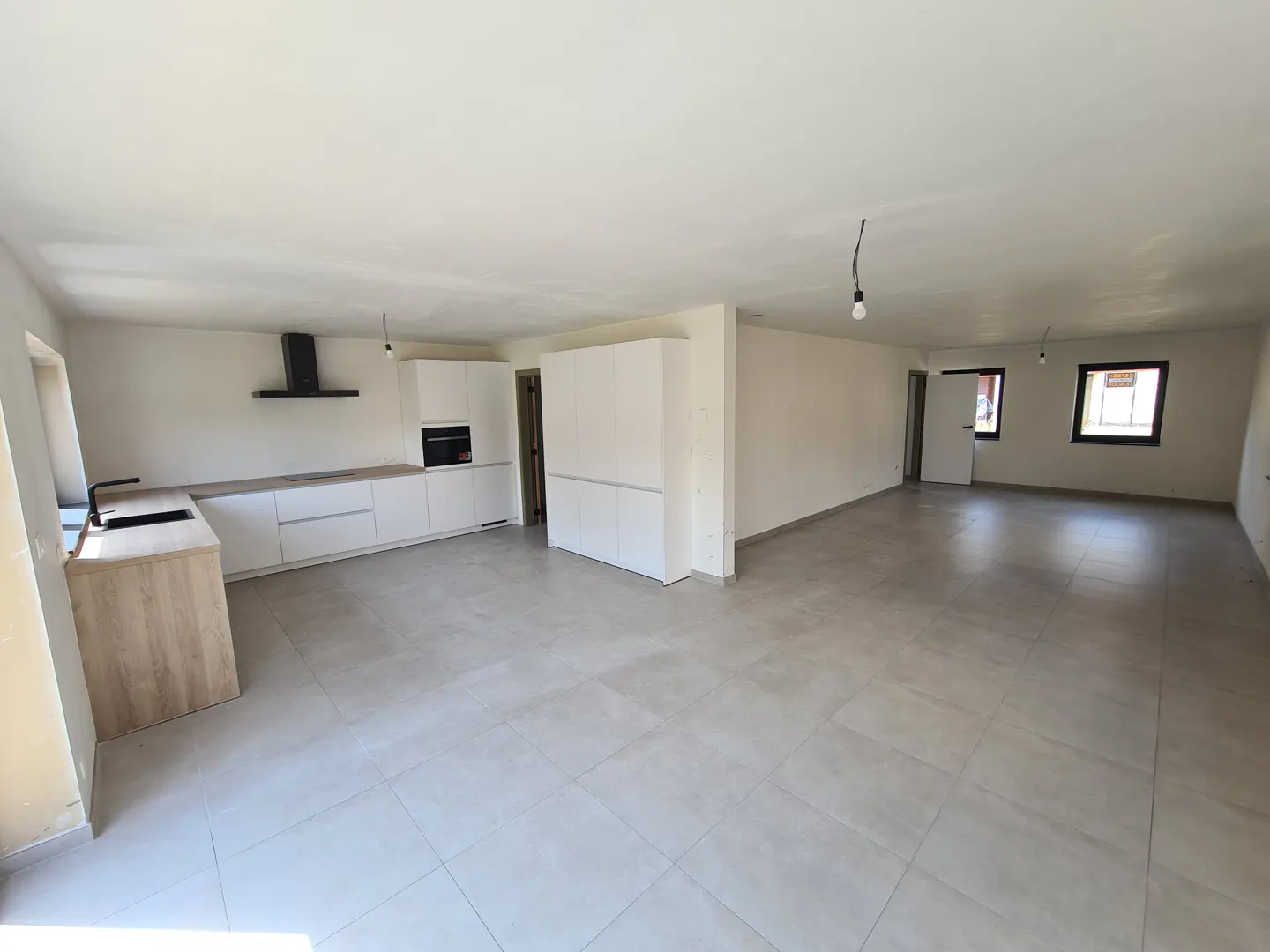 Wide shot of a bright, empty apartment with a modern white kitchen and gray tile flooring.