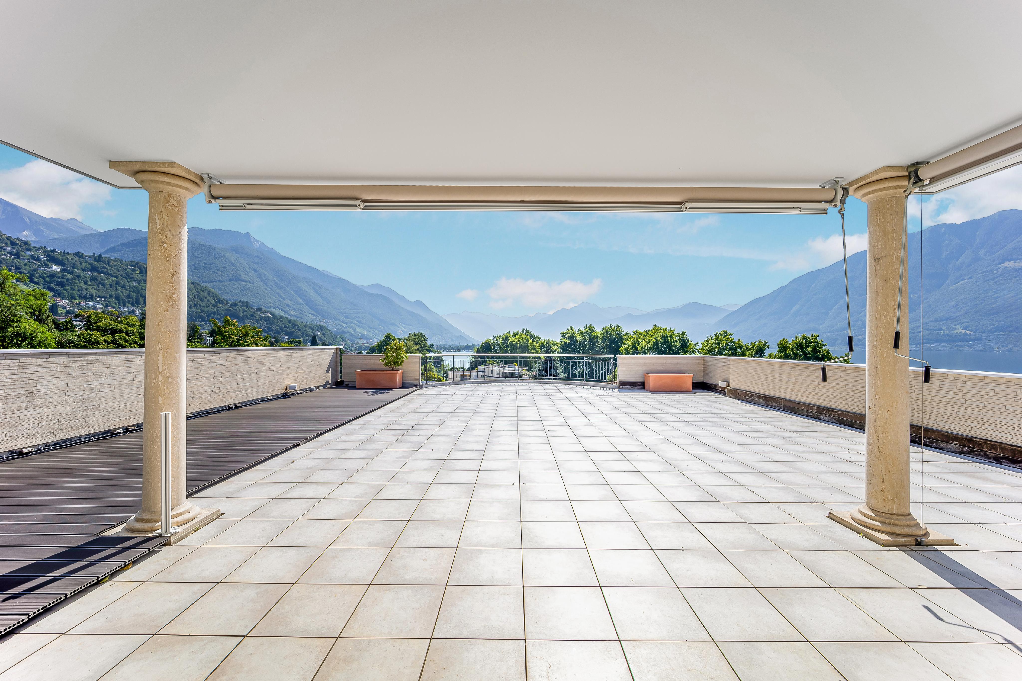 A large, tiled patio with stone columns overlooks a lake and mountains.