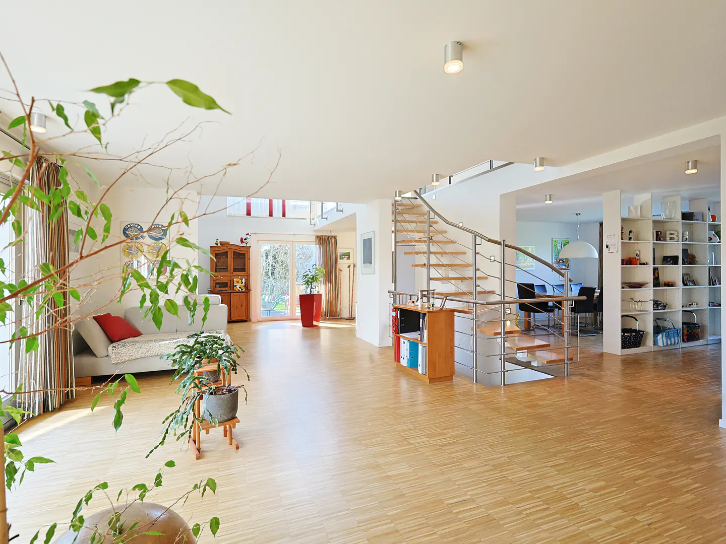Bright, open-concept living room with hardwood floors, white walls, and a spiral staircase. A sofa and plants add warmth to the space.