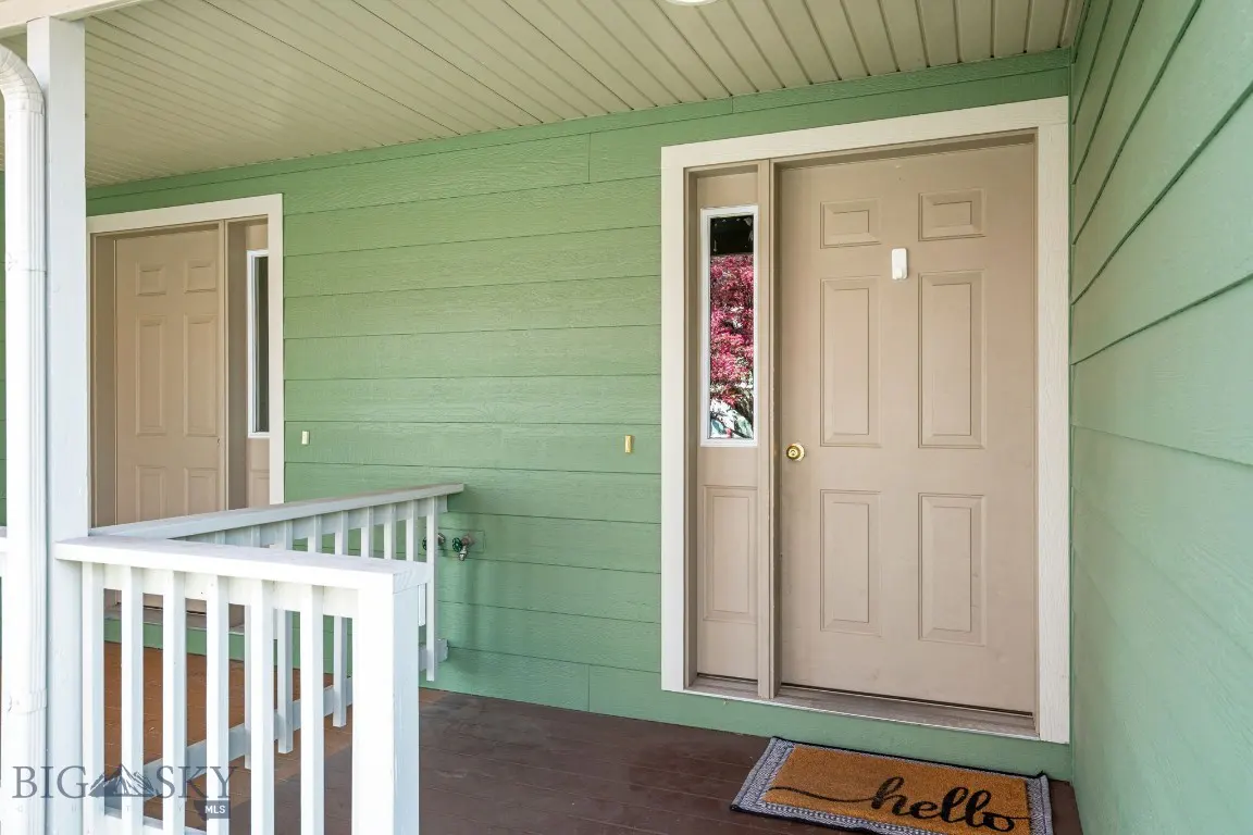 Exterior view of a home's porch with a beige front door, a "hello" doormat, and light green siding.