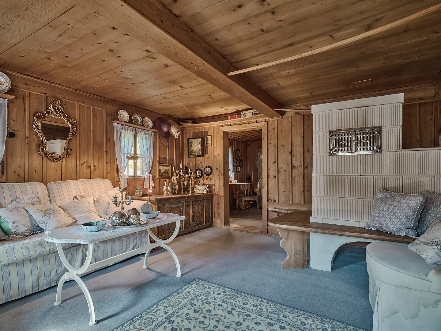 Cozy living room with wood-paneled walls and ceiling, a white sofa, and a tiled fireplace. A blue rug covers the floor.