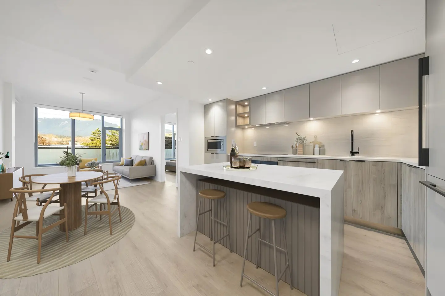 Bright, modern condo interior with a kitchen island, dining table, and living room. Large windows offer a view of trees and mountains.