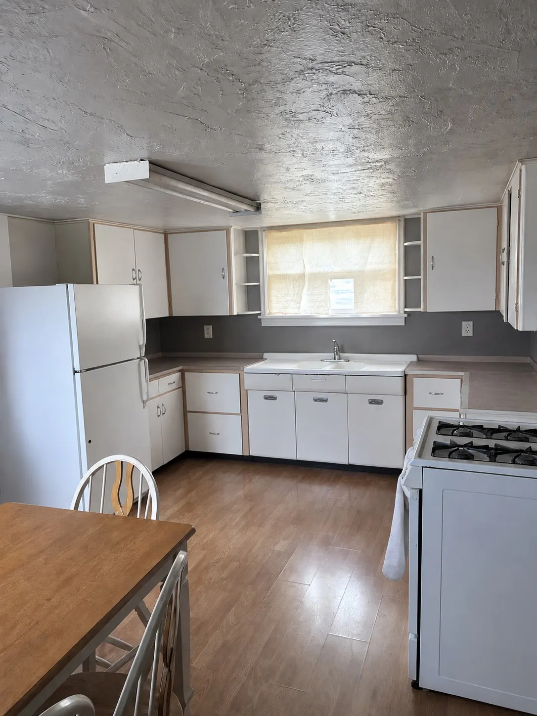 Kitchen with white cabinets, white appliances, wood-look flooring, and a dining table in the foreground.