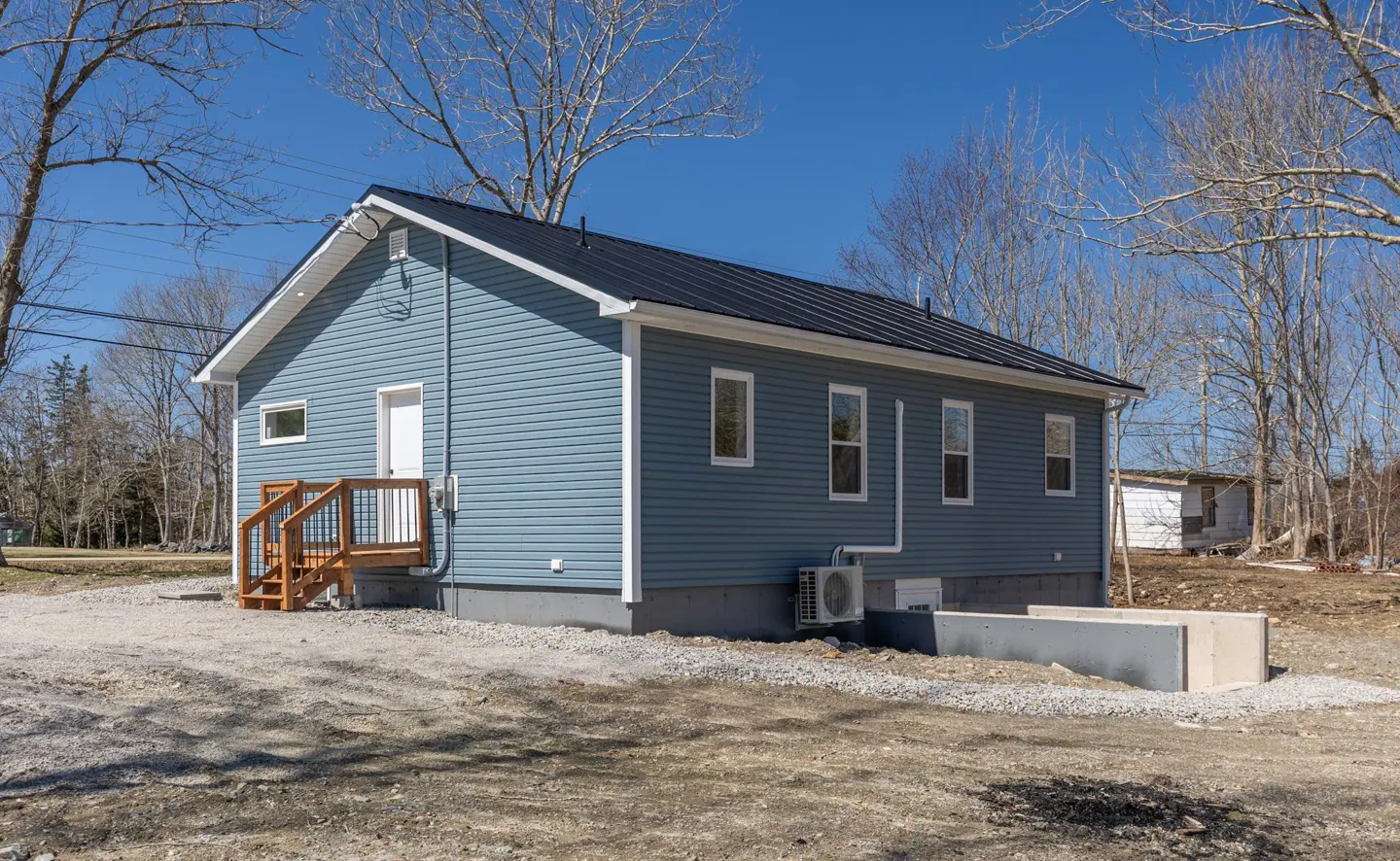 Exterior view of a blue house with a black roof, white trim, and a small wooden deck.