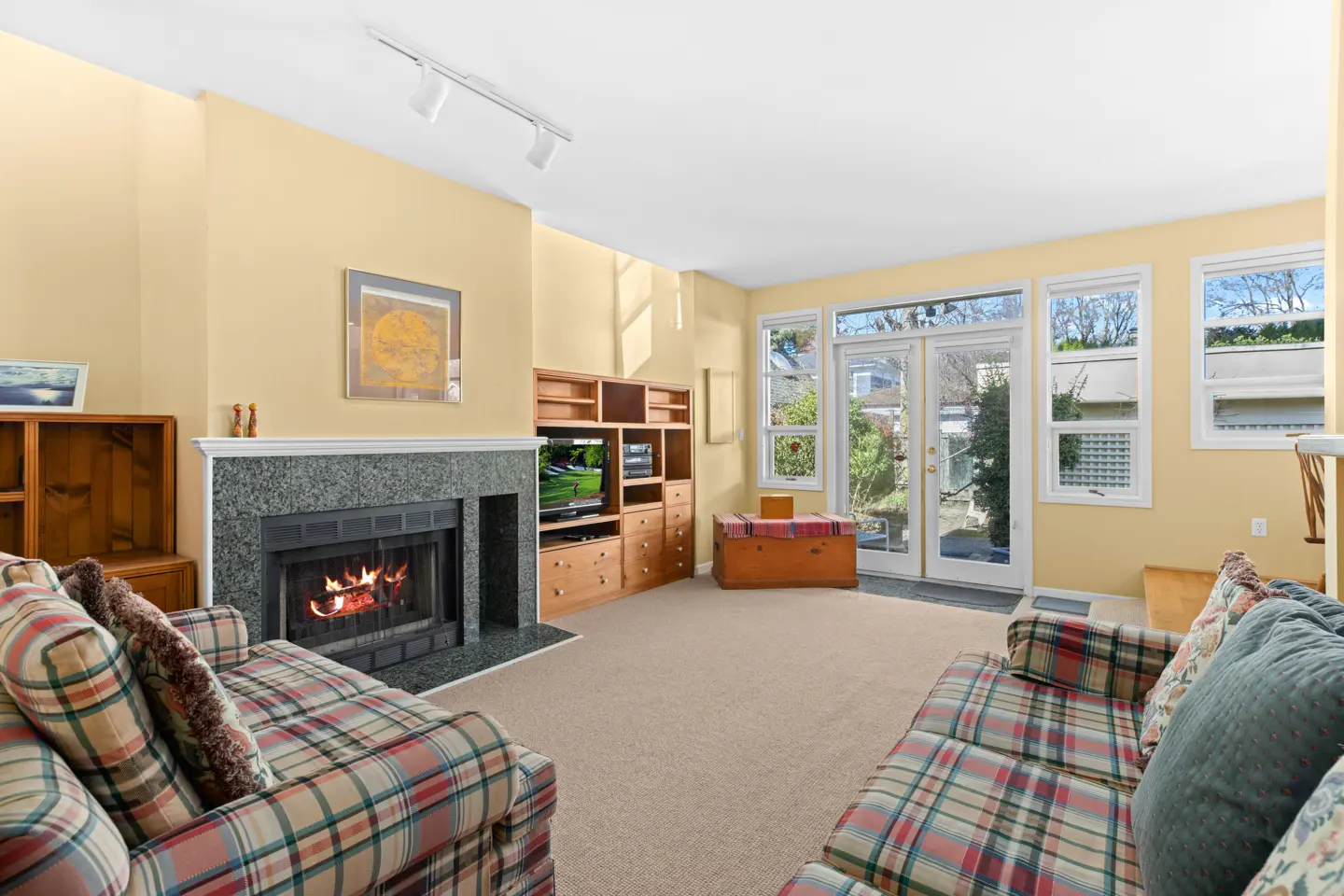 Living room with yellow walls, a fireplace with a granite mantel, and plaid sofas. A built-in entertainment center and a wooden chest are also visible.