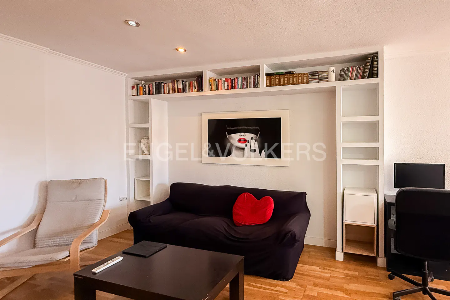 Living room with black sofa, red heart pillow, dark wood table, and white built-in shelves filled with books. A framed art print hangs above the sofa.