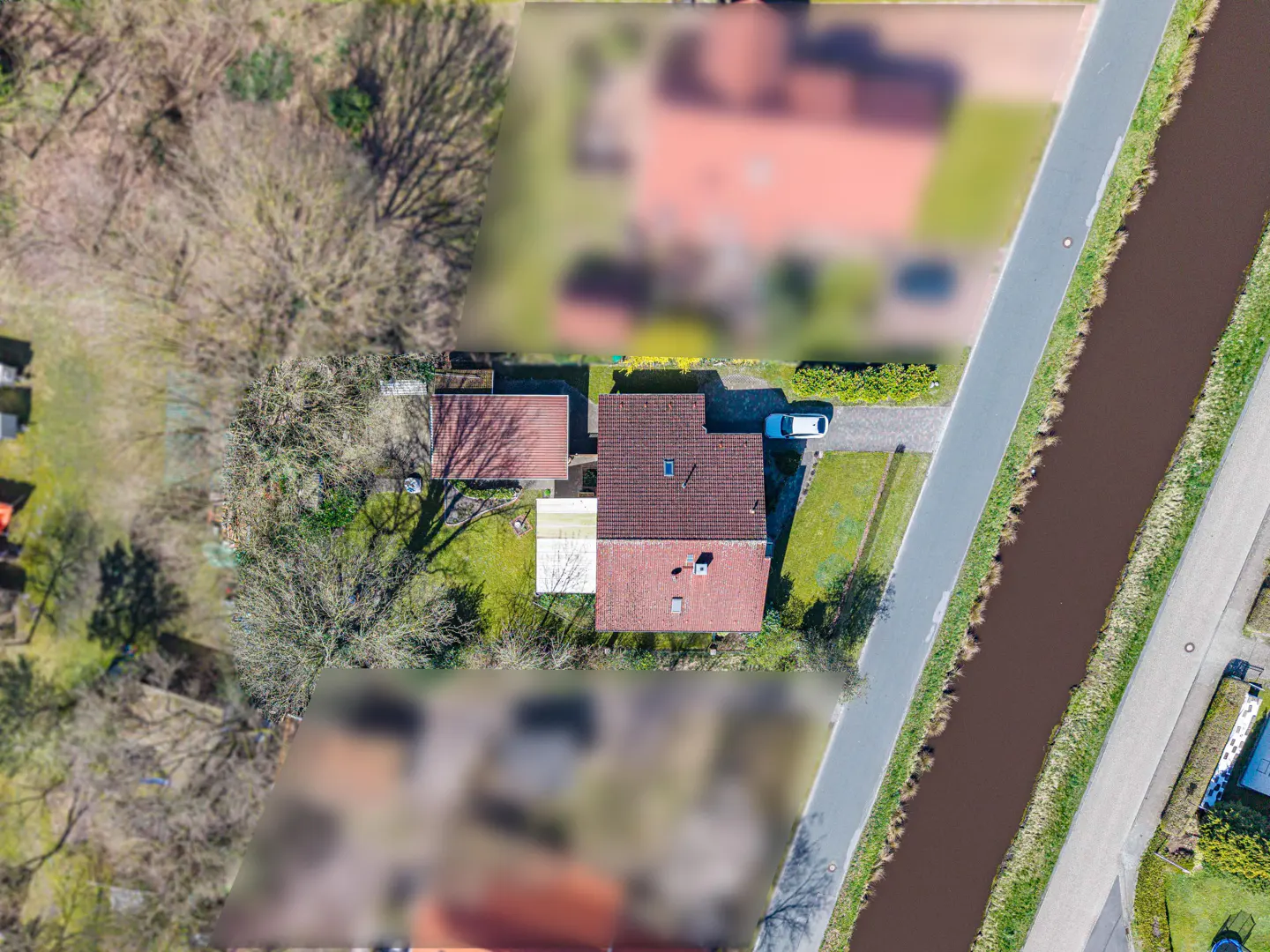 Aerial view of a red-roofed house with a car parked in the driveway, next to a canal and a road.