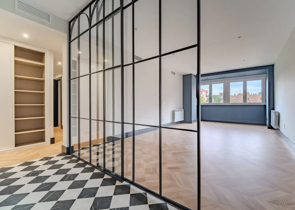 Bright, modern apartment interior with black and white checkered tile floor, black framed glass partition, and light wood floors.