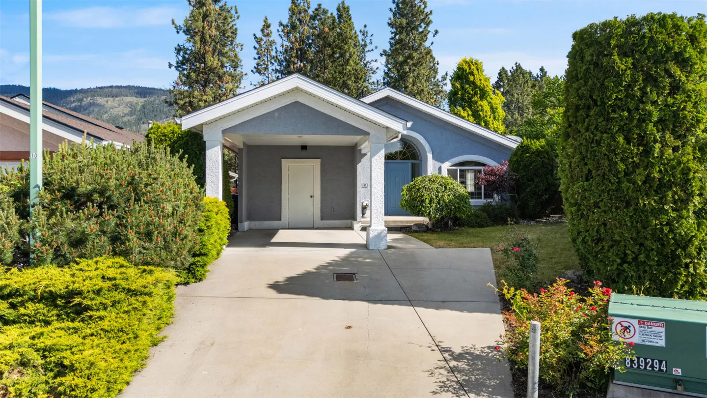 A single-story blue house with a carport and a concrete driveway on a sunny day.