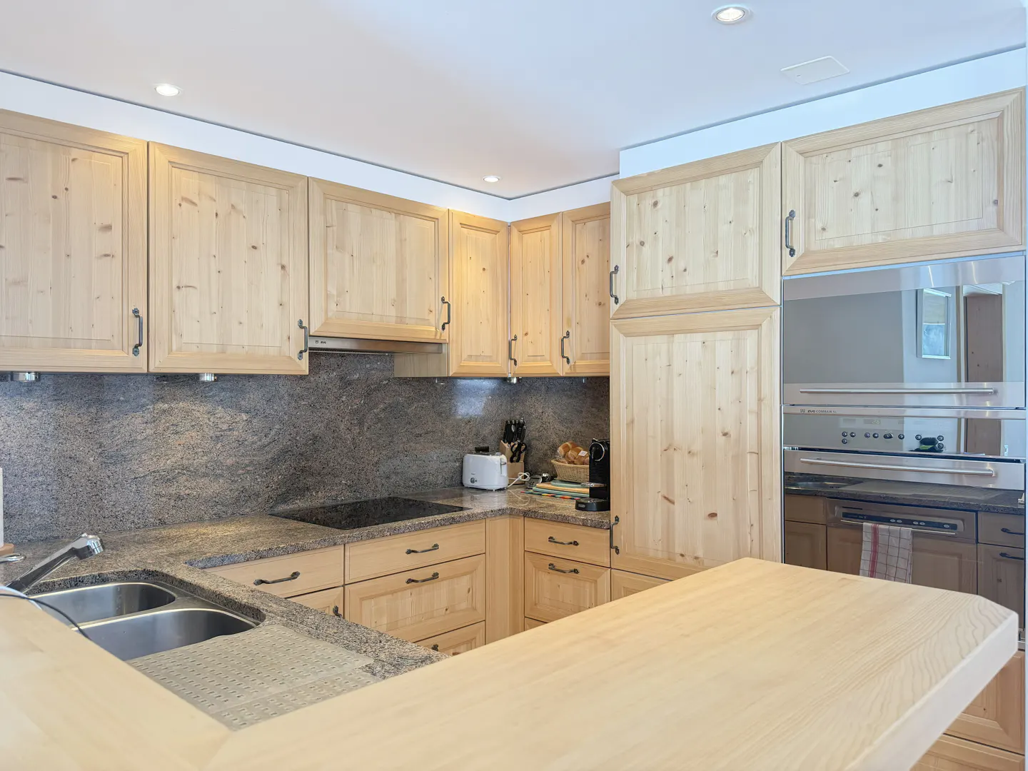 A kitchen with light wood cabinets, granite countertops, and stainless steel appliances.
